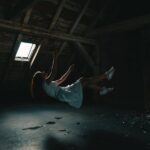 A surreal photograph of a woman in a white dress floating in an abandoned attic, capturing a sense of mystery.