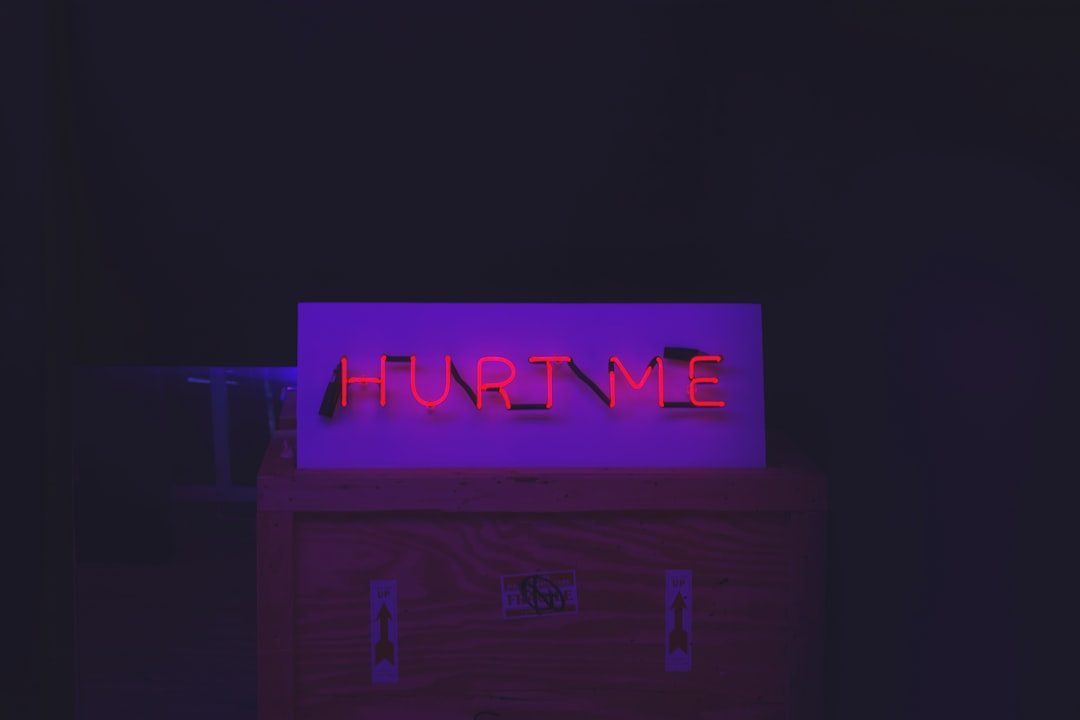 Red neon "Hurt Me" sign on top of a crate with arrow stickers