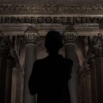 Man stands before ancient roman pantheon at night.