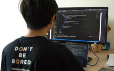 man in black shirt using laptop computer and flat screen monitor
