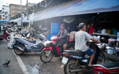 People riding motorcycles in a busy market street.