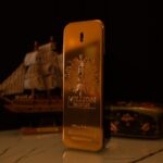 Elegant golden perfume bottle with a ship and floral box in the background.