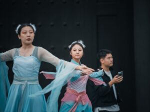 Dancers in traditional chinese attire perform with a man observing.