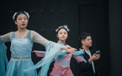 Dancers in traditional chinese attire perform with a man observing.