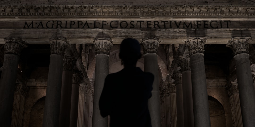 Man stands before ancient roman pantheon at night.