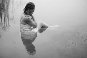 Elegant black and white portrait of a young woman reflecting by the water's edge.