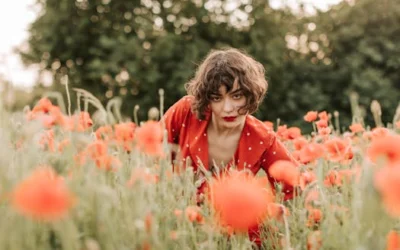 Woman in a red polka dot dress surrounded by vivid poppy flowers outdoors.
