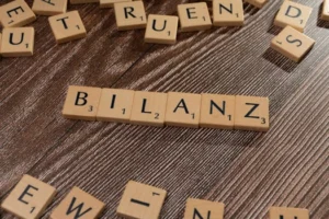 Scrabble tiles spelling 'Bilanz' on a wooden surface, symbolic of financial balance.
