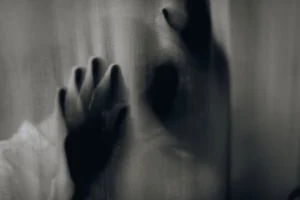 Blurred hands pressed against a curtain creating an eerie silhouette.