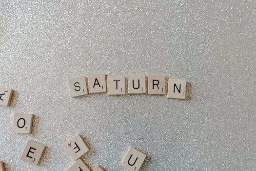 Scrabble tiles forming the word SATURN on a sparkling glitter background, space theme.