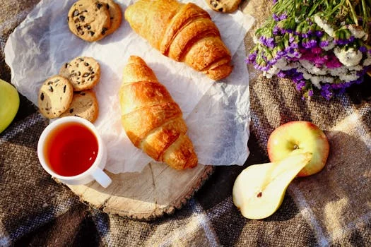 Enjoy a cozy breakfast with croissants, cookies, fruit, and a cup of tea on a rustic table.