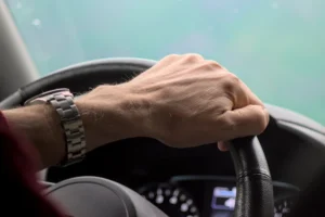 Hand gripping a steering wheel while driving.
