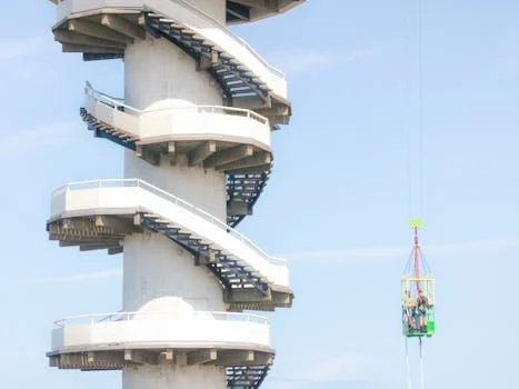 A daring bungy jump beside a striking spiral staircase against a clear blue sky in the Netherlands.