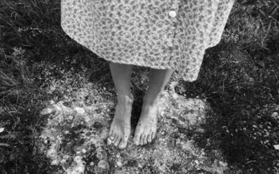 A black and white image showing bare feet on a natural ground outdoors.