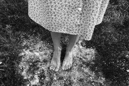 A black and white image showing bare feet on a natural ground outdoors.
