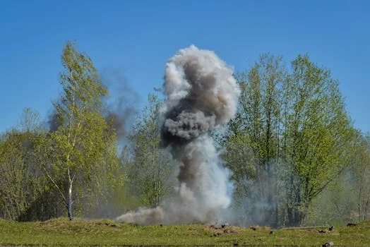 A powerful explosion creates a huge cloud of smoke against a backdrop of green trees, illustrating nature vs. destruction.