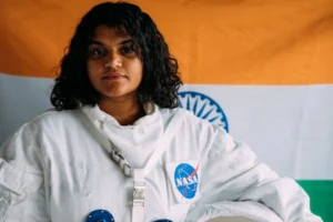 Portrait of an Indian woman wearing a NASA space suit and standing in front of the Indian flag.
