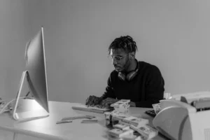 Black and white photo of a focused man typing surrounded by cash indoors.