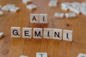 Scrabble tiles spell out the words 'Gemini' and 'AI' on a wooden surface, symbolizing technology and communication.