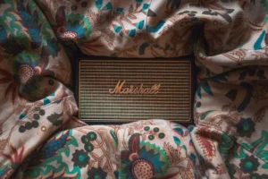 Close-up of a vintage Marshall speaker resting on floral patterned fabric, emphasizing design and texture.
