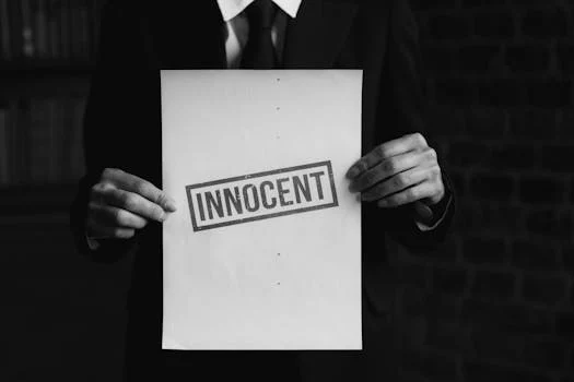 A black and white photo of a person holding a paper with 'INNOCENT' text, conveying a message of legal or moral purity.