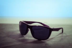 Black sunglasses with dark lenses on a wooden table by the beach offering chic summer protection.