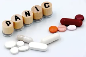 Assorted pills arranged beside wooden tiles spelling 'PANIC', symbolizing anxiety treatment.