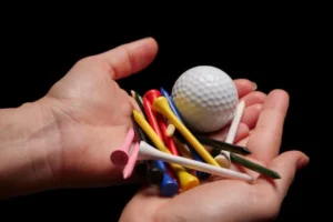 Hands holding a collection of colorful golf tees and a golf ball against a black background.