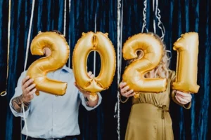 Two people holding golden 2021 balloons, celebrating a festive New Year event.