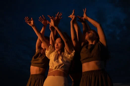 Group of women dancing with raised arms in the evening against a deep blue sky.