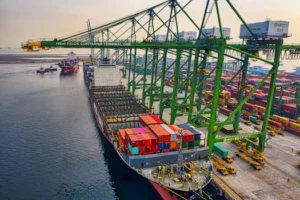 Aerial view of a cargo ship docked at New Priok Container Terminal, Jakarta, showcasing vibrant logistics activity.