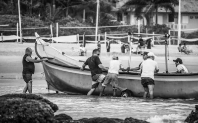 Black and white photo of men pushing a fishing boat onto the beach.