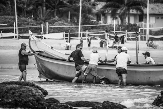 Black and white photo of men pushing a fishing boat onto the beach.