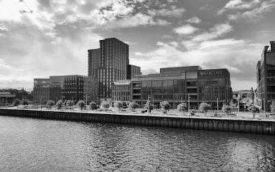 Black and white image showcasing modern architecture along the Glasgow riverside under a cloudy sky.