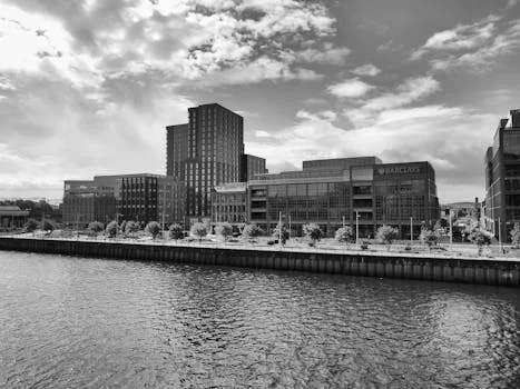 Black and white image showcasing modern architecture along the Glasgow riverside under a cloudy sky.