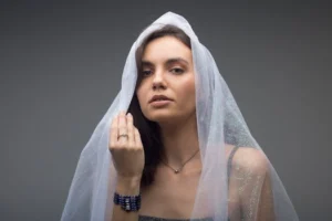 Studio portrait of a woman with a graceful pose under a sheer veil, exuding elegance and mystery.