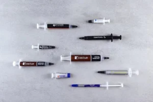 Flat lay of different thermal paste syringes on textured surface for computer hardware.