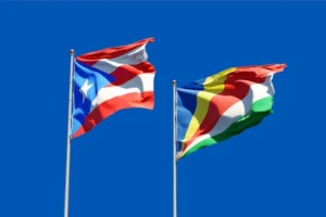 Waving flags of Puerto Rico and Seychelles against a clear blue sky.
