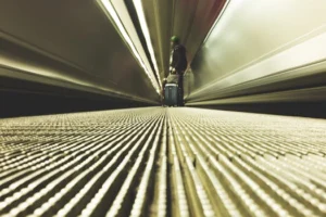 A traveler with luggage on a moving walkway in a modern airport corridor.