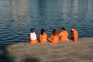 Five people in orange outfits relax by the water on a sunny day.