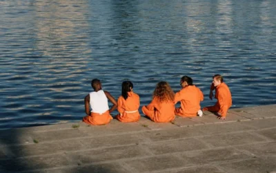 Five people in orange outfits relax by the water on a sunny day.