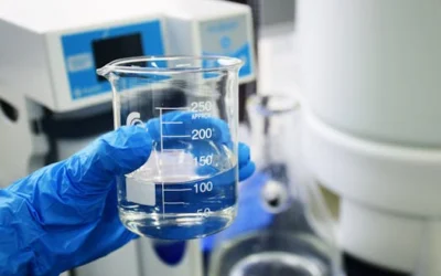 Gloved hand holding a beaker with clear liquid, set against a laboratory background.