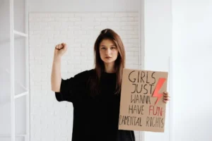 A young woman holds a protest sign advocating for fundamental women's rights indoors.