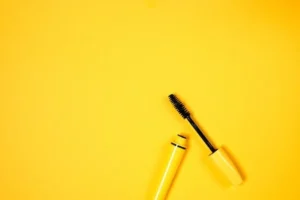 Open mascara with brush on vibrant yellow background, perfect for beauty and cosmetic themes.