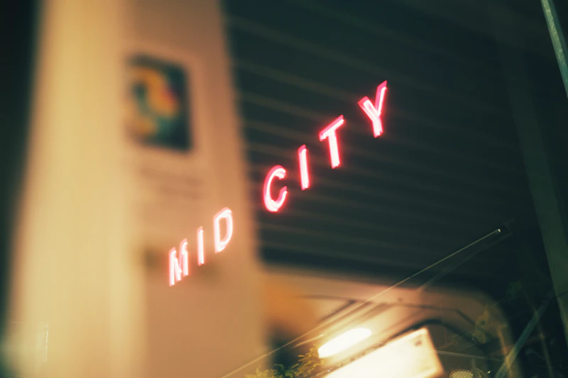 Neon sign reads mid city at night.
