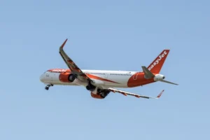 EasyJet airplane captured mid-flight above Prague with a clear blue sky background.