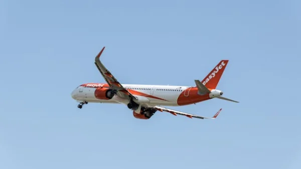EasyJet airplane captured mid-flight above Prague with a clear blue sky background.