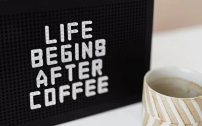 Peg message board with Life Begins After Coffee motto and empty ceramic cup of coffee with creative striped design on white table