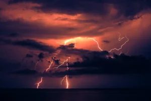 Dramatic lightning strike illuminating dark clouds over the ocean at night, showcasing nature's power.