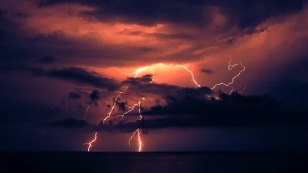 Dramatic lightning strike illuminating dark clouds over the ocean at night, showcasing nature's power.